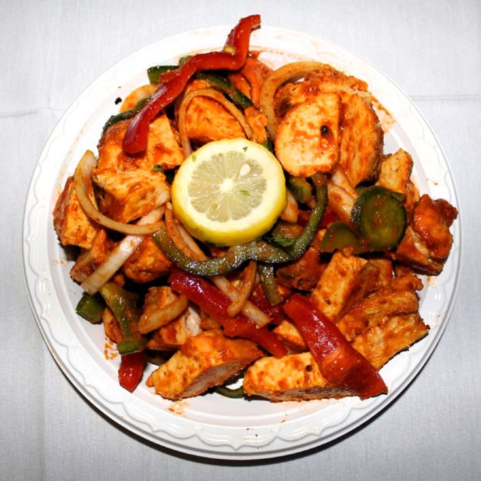 Indian chicken dish with red and green peppers, onions, and a lemon slice on a white plate.